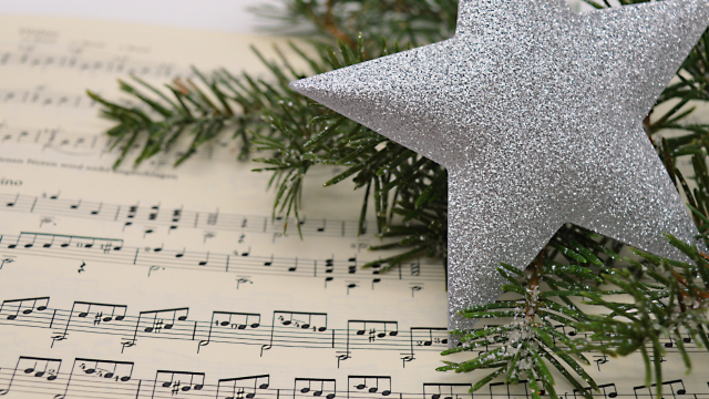 Glitzernder silberner Stern auf Musiknoten und Tannengrün.